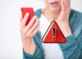Pessoa preocupada segurando celular vermelho ao receber alerta de golpe digital