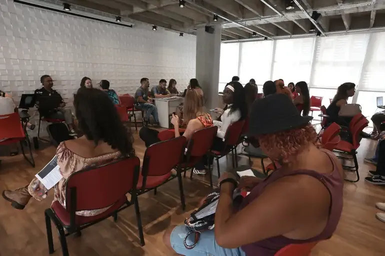 "Grupo de pessoas aguardando atendimento em um local com cadeiras organizadas, em ambiente de atendimento comunitário."