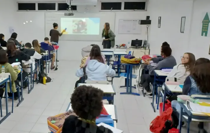 Sala de aula com alunos assistindo a uma apresentação sobre o auxílio para estudantes de cursinhos populares.