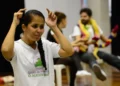 Mulher fazendo interpretação em Libras, com pessoas ao fundo, representando inclusão e acessibilidade.