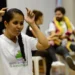 Mulher fazendo interpretação em Libras, com pessoas ao fundo, representando inclusão e acessibilidade.