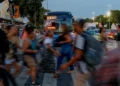 Pessoas apressadas atravessando a rua em meio a um trânsito intenso, ilustrando o cotidiano de trabalho e impostos pesados.