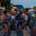 Pessoas apressadas atravessando a rua em meio a um trânsito intenso, ilustrando o cotidiano de trabalho e impostos pesados.