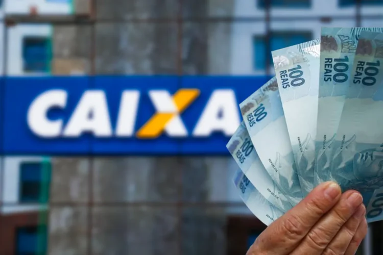 Mão segurando notas de 100 reais em frente à agência da Caixa Econômica Federal.