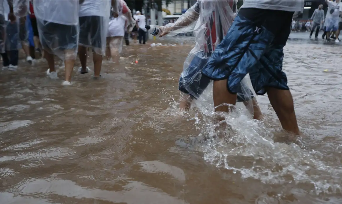 Pessoas andando em rua alagada durante enchente, ilustrando situação de calamidade em áreas afetadas pelo Bolsa Família.