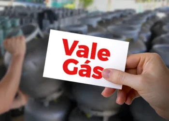 Cartão com os dizeres "Vale Gás" sendo segurado por uma mão, com botijões ao fundo