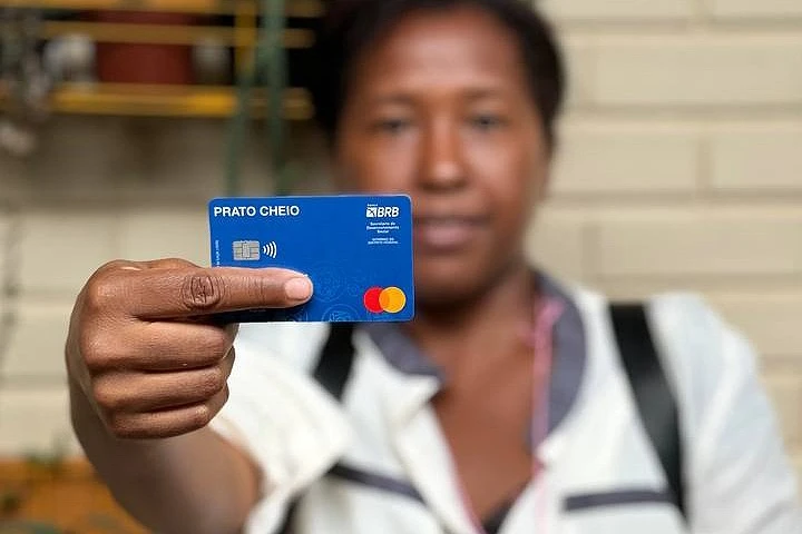 Cartão Prato Cheio em destaque na mão de uma mulher, com fundo desfocado.