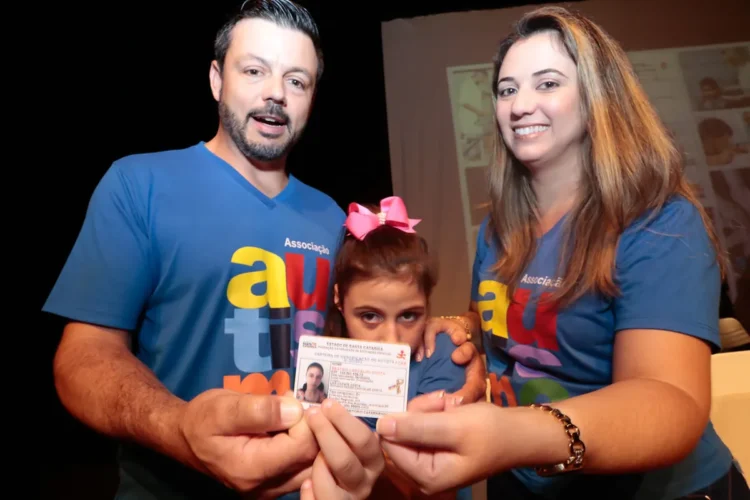 Família feliz segurando a Carteira de Identificação do Autista, mostrando a importância do documento.