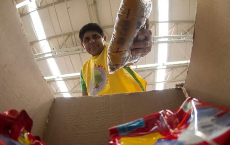 Homem colocando alimentos em uma caixa, representando o aumento dos preços da cesta básica.