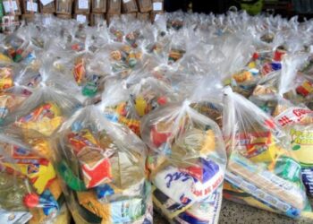 Diversas cestas básicas embaladas em sacos plásticos transparentes, prontas para distribuição.