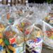 Diversas cestas básicas embaladas em sacos plásticos transparentes, prontas para distribuição.