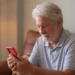 Homem idoso usando celular com atenção, representando cuidados ao navegar na internet.