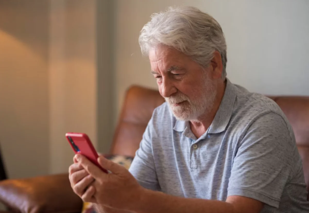 Homem idoso usando celular com atenção, representando cuidados ao navegar na internet.