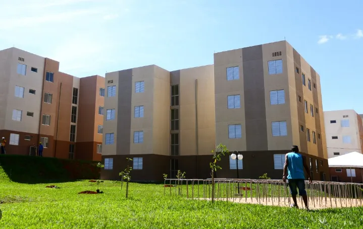 Prédios residenciais do programa Aluguel Social 2025 com área verde e pessoa caminhando