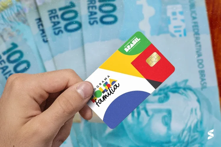 Cartão do Bolsa Família com cédulas de R$ 100 ao fundo.