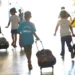 Crianças andando em corredor de escola com mochilas de rodinhas, vista de costas.