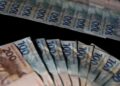Cédulas brasileiras de 100 e 200 reais dispostas em leque sobre fundo preto, representando o dinheiro do Pé-de-Meia.