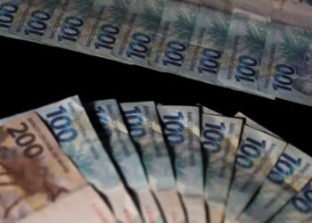 Cédulas brasileiras de 100 e 200 reais dispostas em leque sobre fundo preto, representando o dinheiro do Pé-de-Meia.