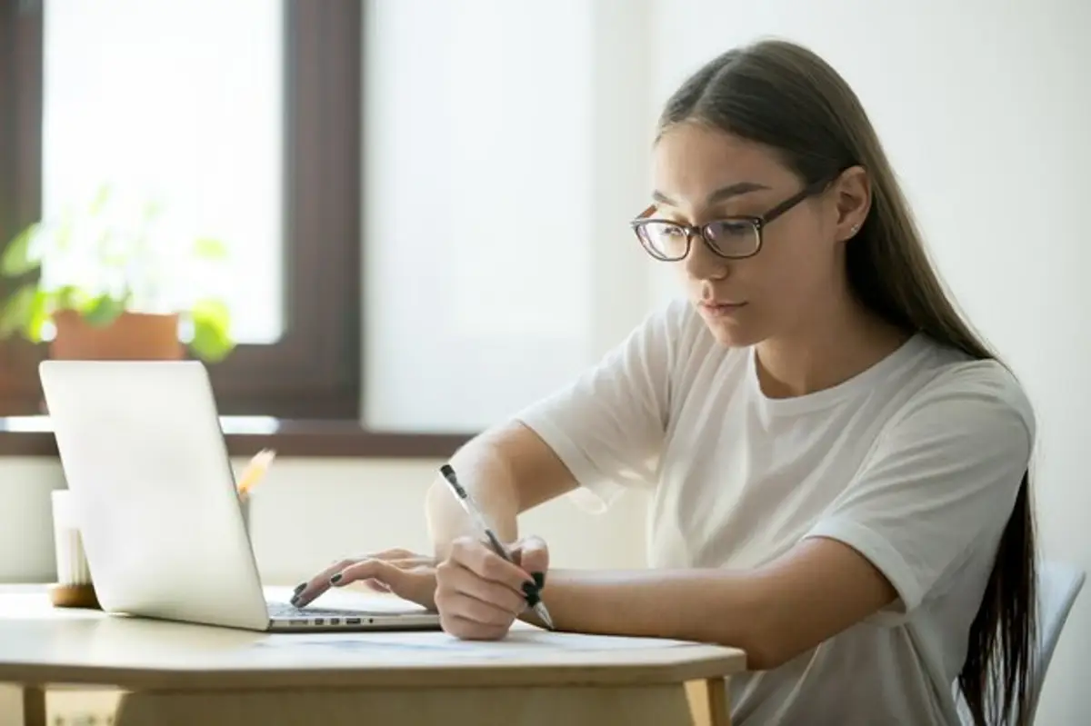 Estudante com óculos estudando no computador para o Enem 2025.
