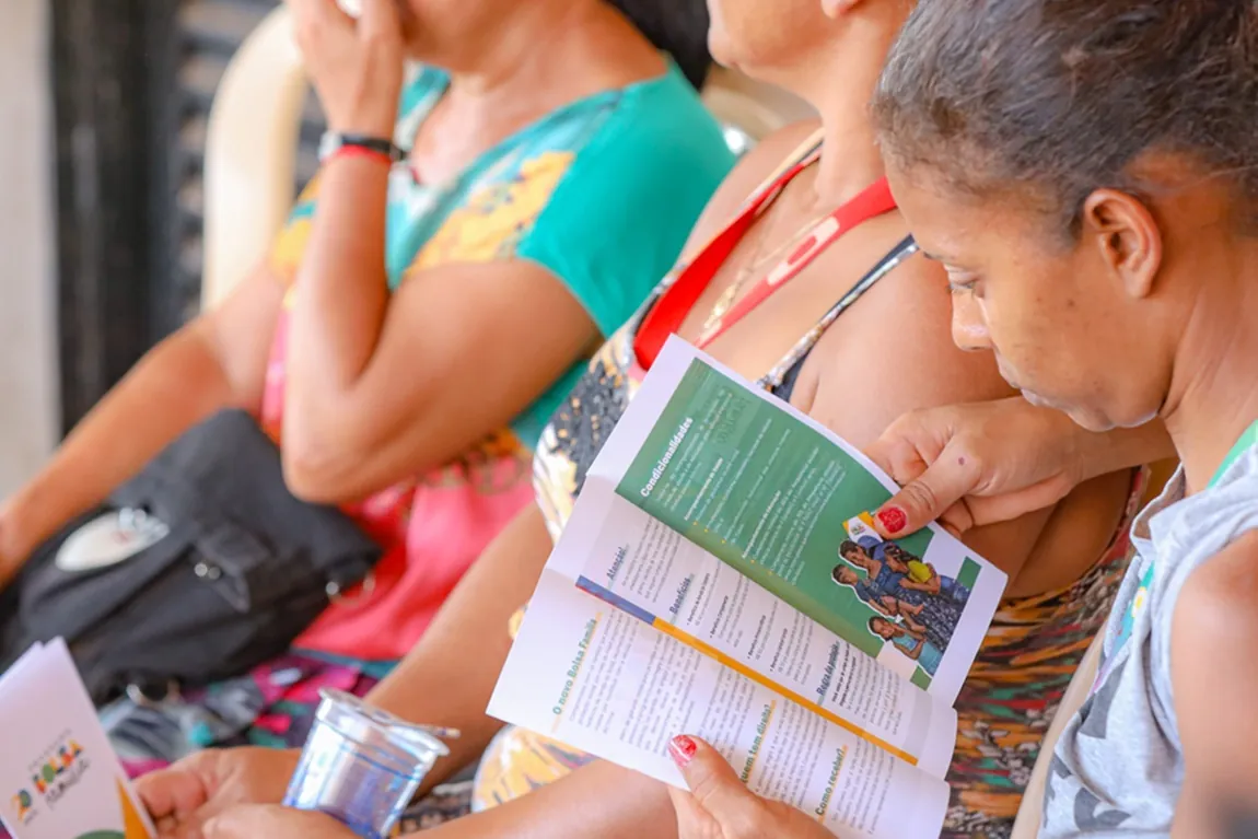 Mulheres lendo cartilha informativa do Bolsa Família durante atendimento social.