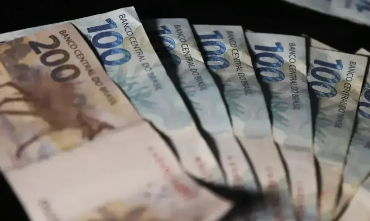 Notas de R$ 100 e R$ 200 dispostas em um fundo preto, representando o valor de R$ 1.518,00 em dinheiro.