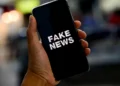Mão segurando smartphone com a tela exibindo a mensagem "Fake News"
