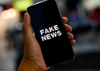 Mão segurando smartphone com a tela exibindo a mensagem "Fake News"
