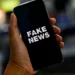 Mão segurando smartphone com a tela exibindo a mensagem "Fake News"