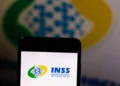 Logo do INSS exibido na tela de um smartphone com fundo desfocado, em referência à suspensão de novos empréstimos consignados.