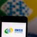 Logo do INSS exibido na tela de um smartphone com fundo desfocado, em referência à suspensão de novos empréstimos consignados.