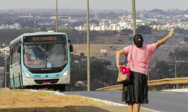 Mulher acenando para ônibus em via urbana com cidade ao fundo