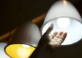 Mão se aproximando de uma luminária pendente com lâmpada acesa.