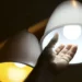 Mão se aproximando de uma luminária pendente com lâmpada acesa.
