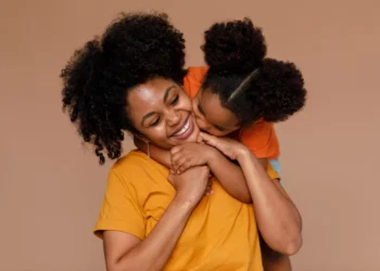 Mãe e filha sorrindo juntas em um abraço carinhoso, com um fundo suave de cor quente.