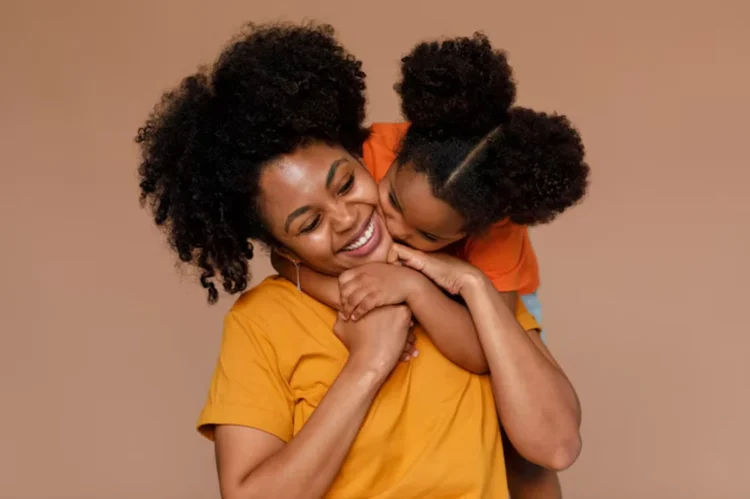 Mãe e filha sorrindo juntas em um abraço carinhoso, com um fundo suave de cor quente.