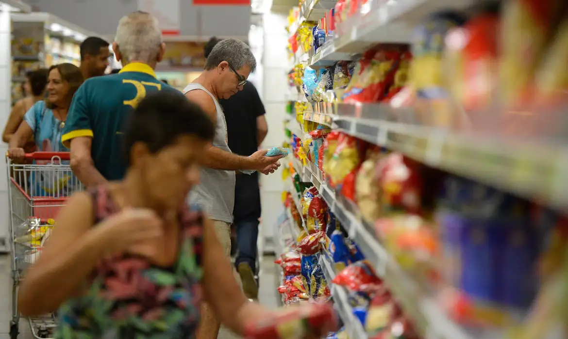  Pessoas fazendo compras em supermercado, comparando produtos e preços nas prateleiras.