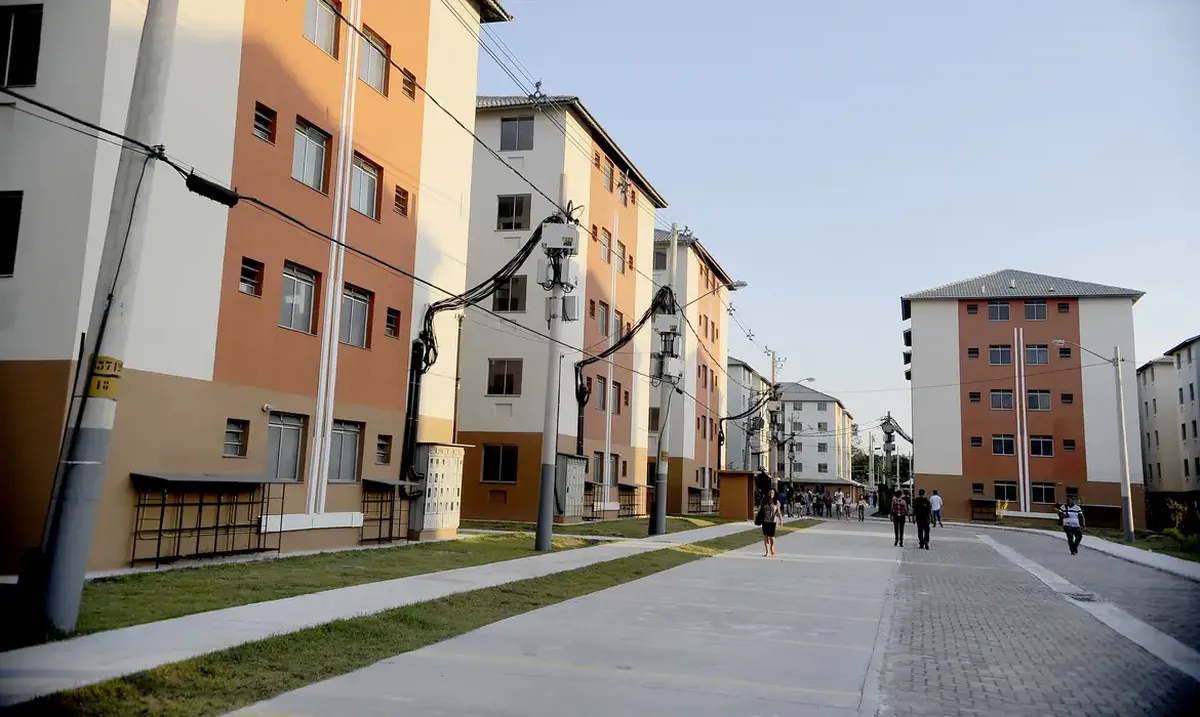 Bloco de apartamentos do programa Minha Casa Minha Vida com moradores caminhando na área comum.