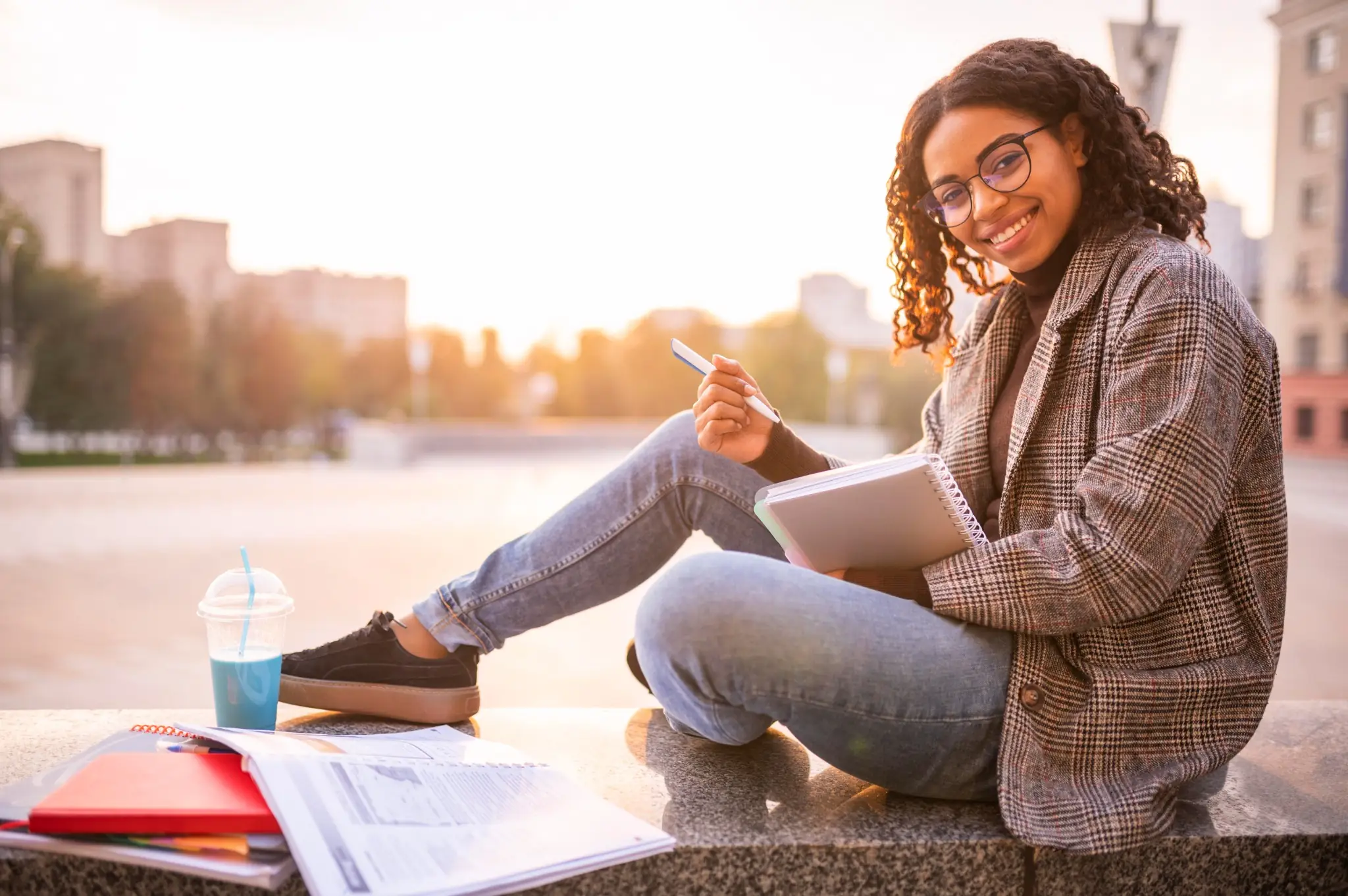 Estudante sorrindo enquanto faz os estudos ao ar livre, simbolizando o pagamento do Pé-de-Meia para o mês de maio.