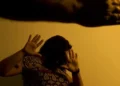 Mulher protegendo o rosto com as mãos em sinal de defesa contra violência doméstica.