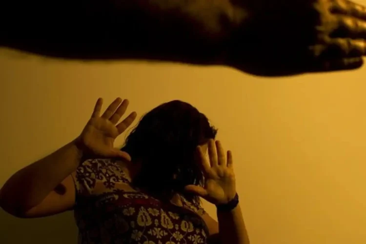 Mulher protegendo o rosto com as mãos em sinal de defesa contra violência doméstica.