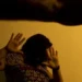 Mulher protegendo o rosto com as mãos em sinal de defesa contra violência doméstica.