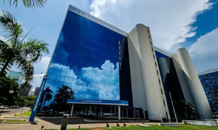 Prédio do INSS refletindo o céu, com a fachada principal da Previdência Social em destaque.