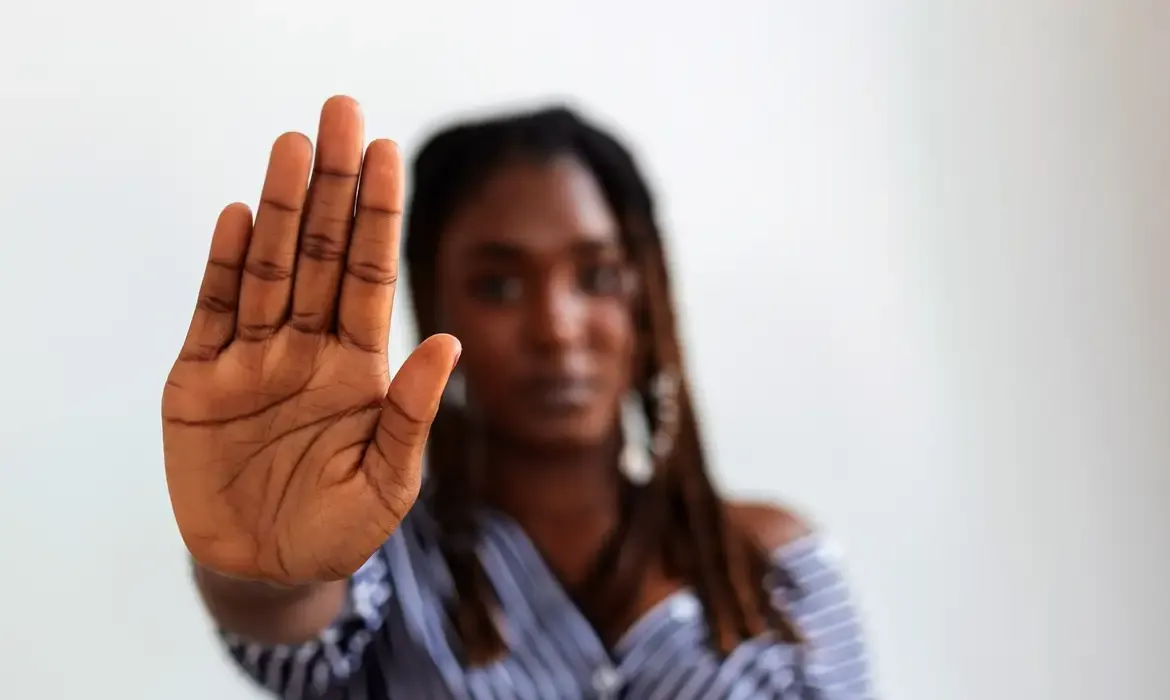  Mulher com a mão levantada em gesto de pare, simbolizando enfrentamento à violência
