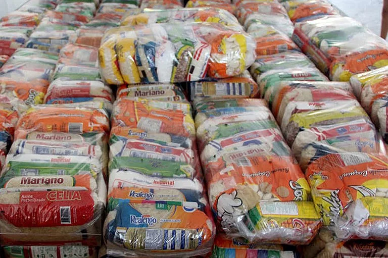 Pilhas de cestas básicas embaladas com alimentos diversos, prontas para distribuição.