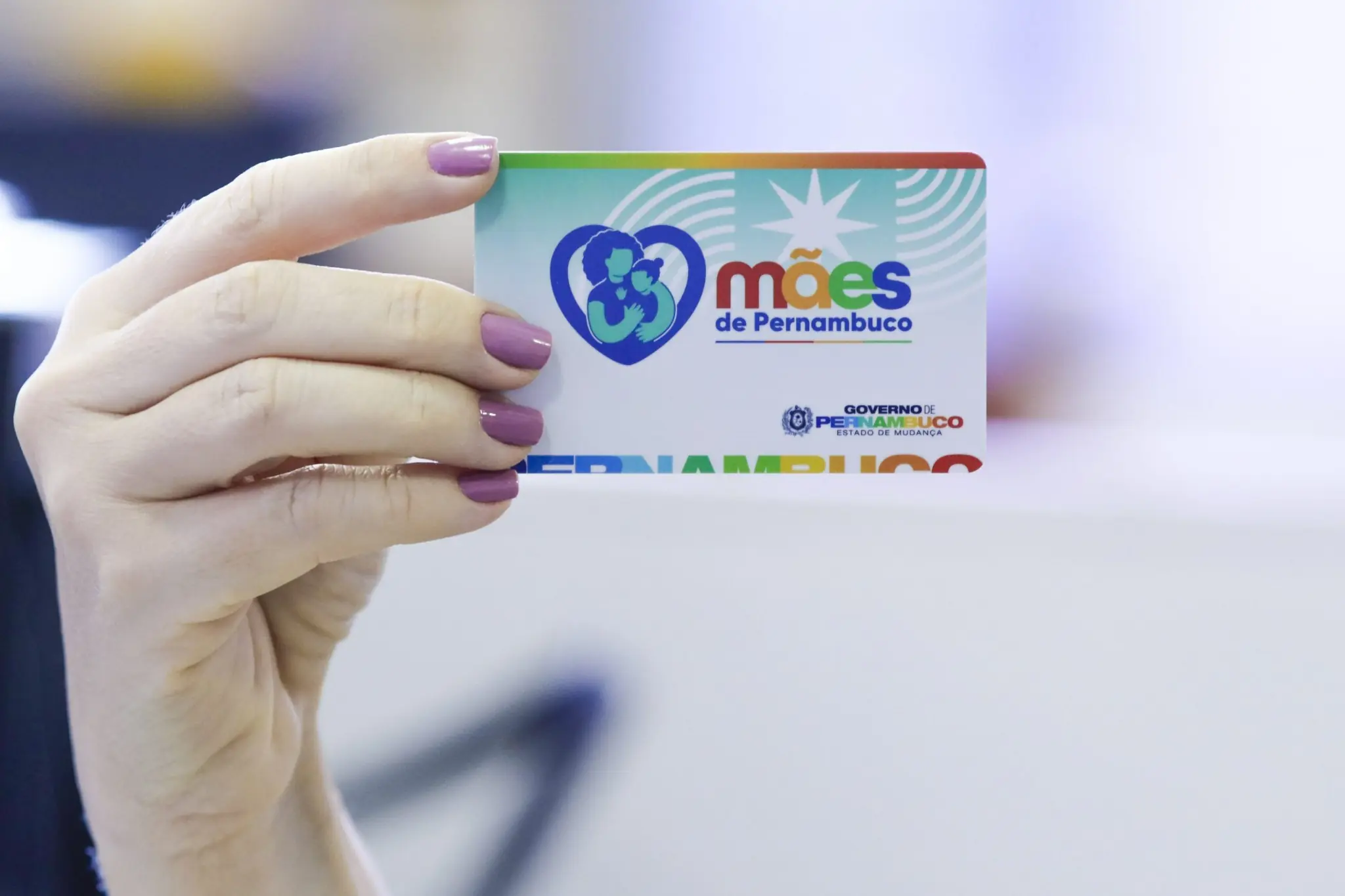 Mulher segurando o cartão do programa Mães de Pernambuco, destinado às beneficiárias do auxílio de R$ 300.