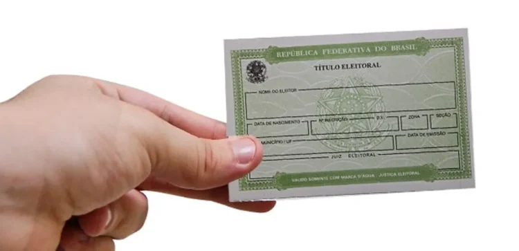 Cartão de título eleitoral brasileiro sendo segurado por uma mão, simbolizando a importância da regularização do título de eleitor.