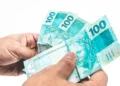 Notas de R$ 100 do Brasil sendo seguradas, ilustrando o valor do 13º salário.