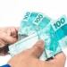 Notas de R$ 100 do Brasil sendo seguradas, ilustrando o valor do 13º salário.