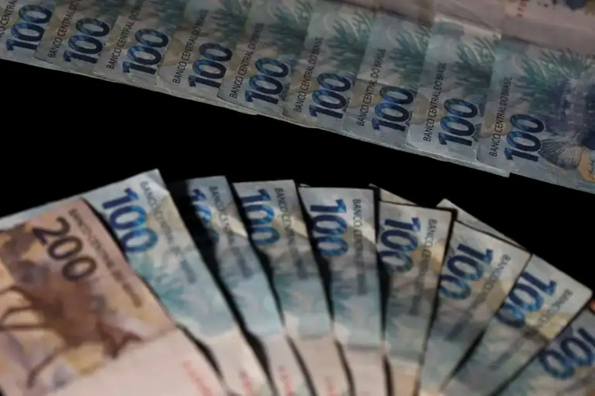 Notas de 100 e 200 reais organizadas em leque sobre fundo preto.
