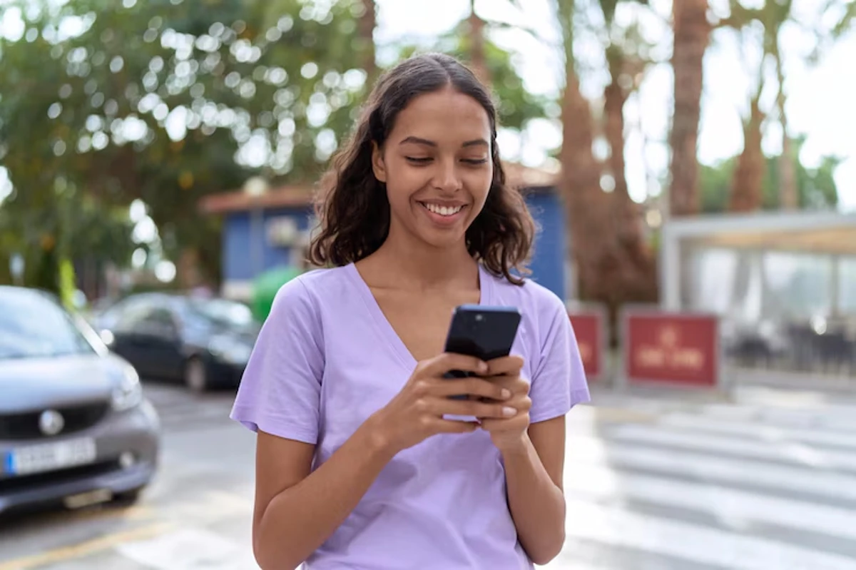 Mulher sorridente conferindo aprovação de isenção pelo celular ao ar livre